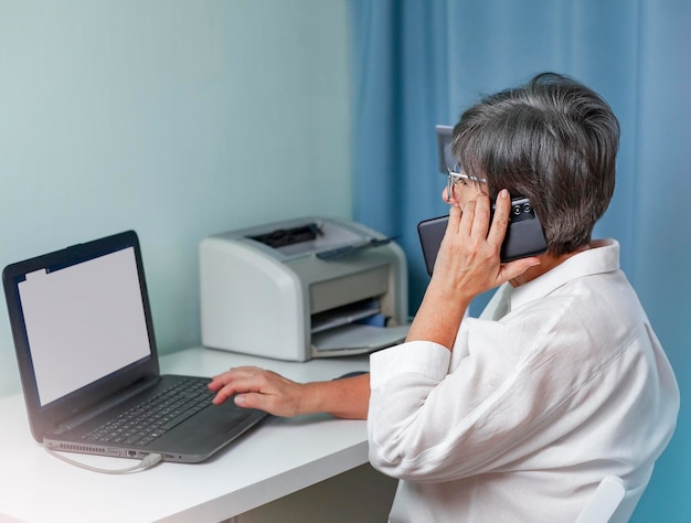 Frau sitzt am Telefon und arbeitet an einem Laptop