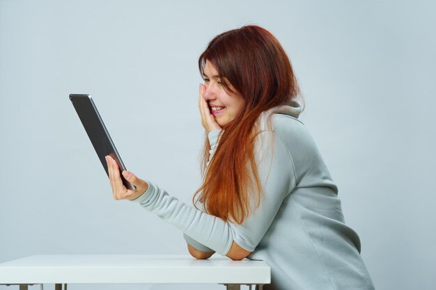 Frau sitzt am Tisch und verwendet Tablet-Computer für die Kommunikation im Chat oder Video-Chat Social-Media-Konzept