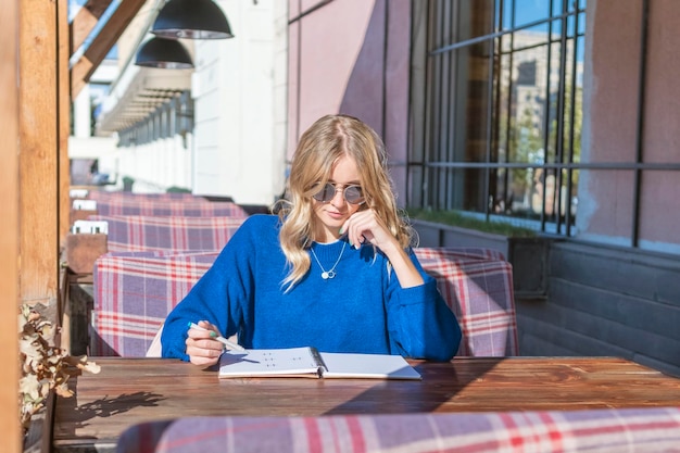 Frau sitzt an einem Tisch in einem Café mit einem offenen Notizbuch auf dem Tisch