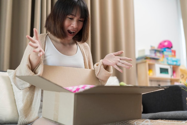 Frau sitzt auf Couch schreiend vor Freude öffnet Karton glückliches Adressatenmädchen erhält lang ersehntes Paket