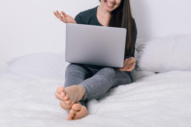 Frau sitzt auf dem Bett und benutzt ihren Laptop