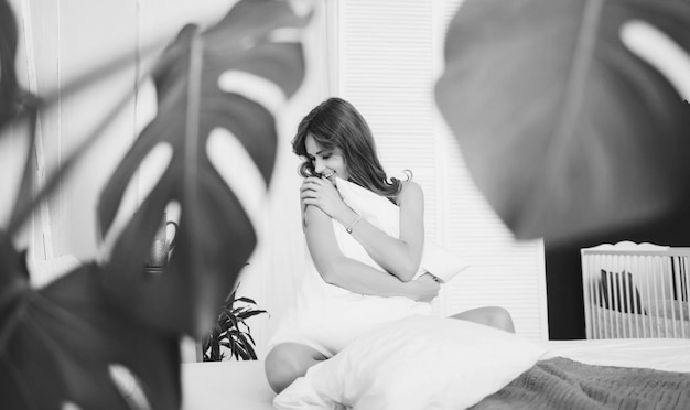 Frau sitzt auf dem Bett und umarmt weißes Kissen