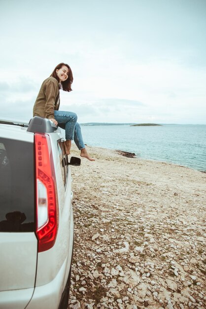 Frau sitzt auf dem dach des autos und genießt den blick auf das meer. roadtrip im sommerurlaub