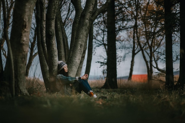 Frau sitzt auf dem Land gegen einen Baumstamm im Wald