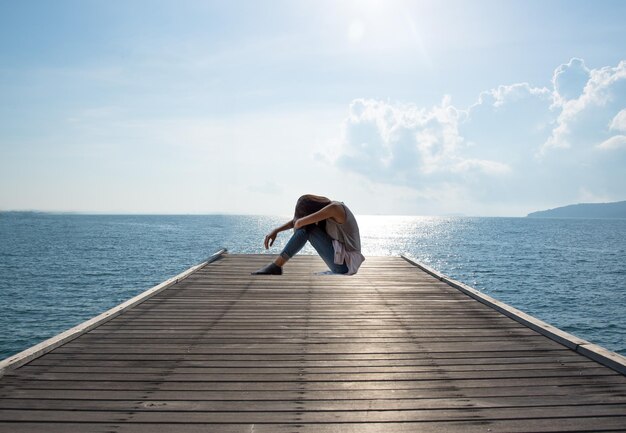 Foto frau sitzt auf dem pier über dem meer gegen den himmel