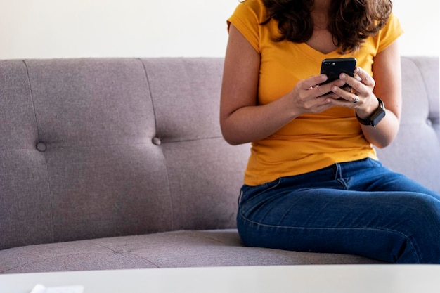 Frau sitzt auf dem Sofa mit Handy in der Hand