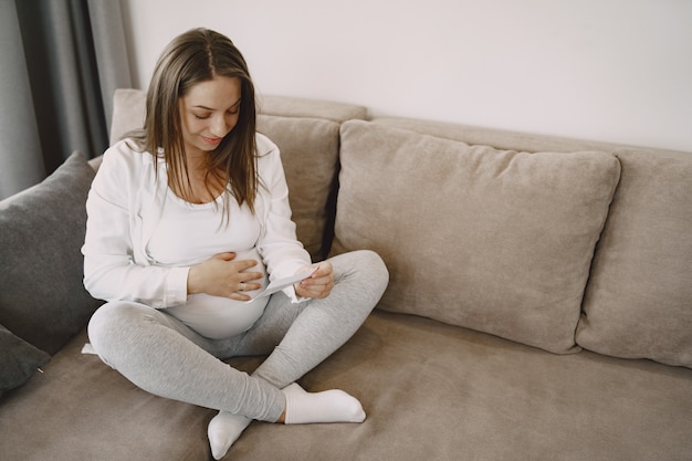 Frau sitzt auf der Couch. Schwangeres Betrachten des Fotos. Mutter erwartet ein Baby.