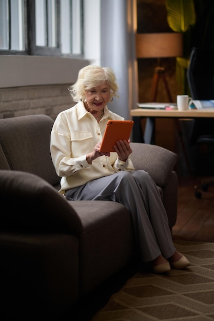 Frau sitzt auf der Couch und schaut auf das Tablet.