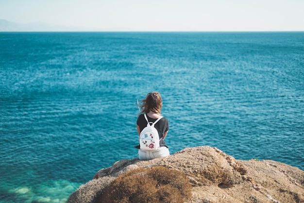 Frau sitzt auf einem Felsen vor dem Meer