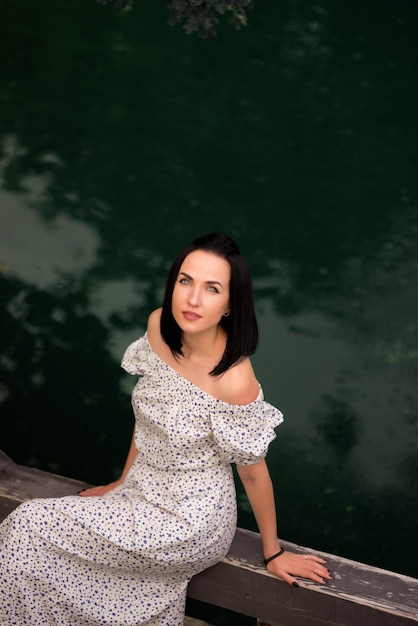Frau sitzt auf einem Pier vor einem grünen Wasser.