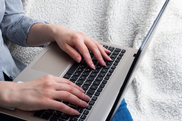 Frau sitzt auf einem Sofa, das an Computerhänden arbeitet. Nahansicht.