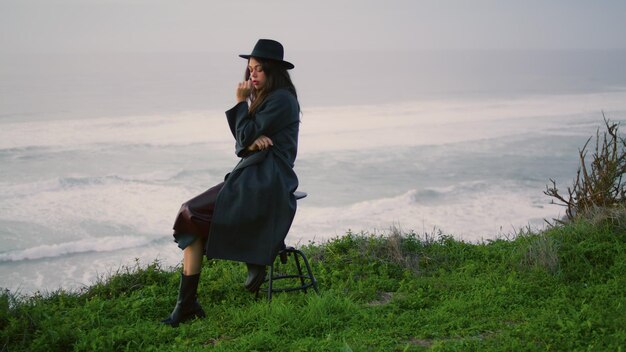Frau sitzt auf einem Stuhl am Meeresufer vor Meereswellen und posiert abends als Model