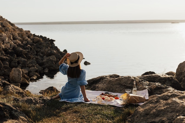 Frau sitzt auf einer Decke vor einem See und genießt ein Picknick.