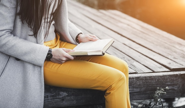 Frau sitzt auf Holzbrücke und hält ein Buch