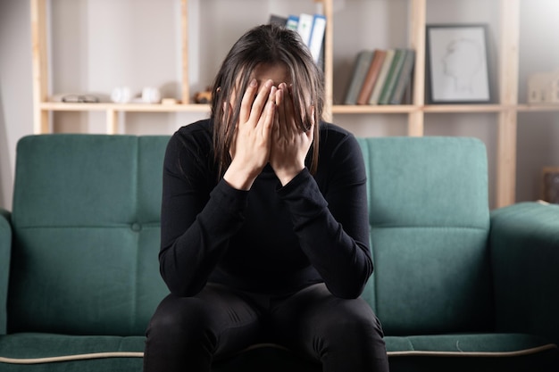 Frau sitzt auf Sofa und bedeckt ihr Gesicht