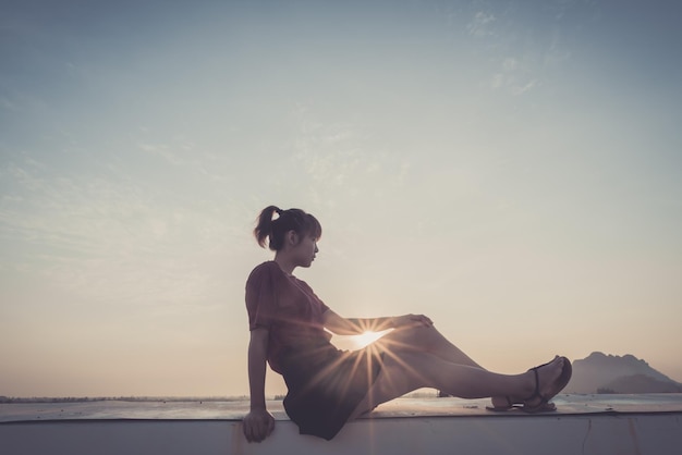 Frau sitzt bei Sonnenuntergang auf einer Stützmauer gegen den Himmel