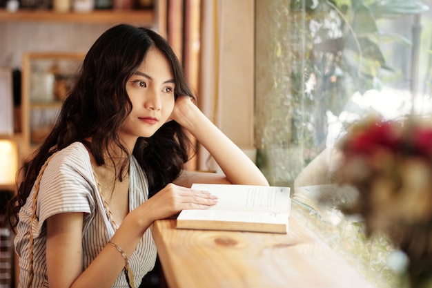 Frau sitzt im Café mit aufgeschlagenem Buch