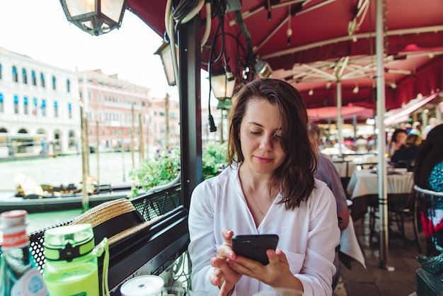 Frau sitzt im Café-Restaurant und schaut ins Telefon und wartet auf Essen Canal Grande in Venedig