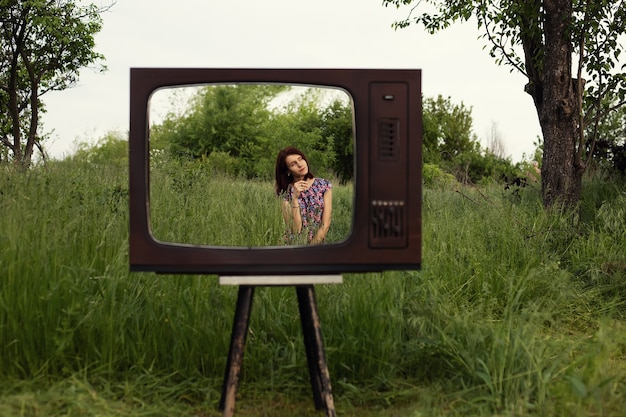 Frau sitzt im Gartengras in einem alten Fernsehrahmen, moderner Technologie und psychischer Gesundheit