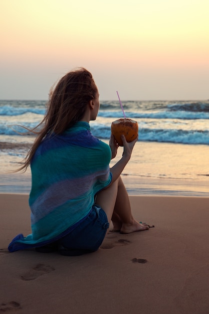 Frau sitzt mit einer Kokosnuss am Meer