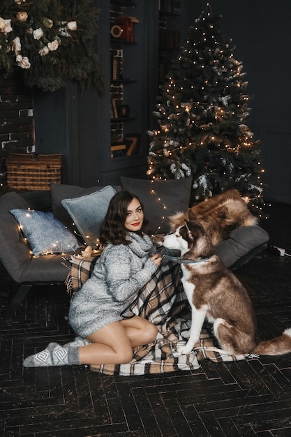 Frau sitzt mit Husky am Sofa und am Weihnachtsbaum.