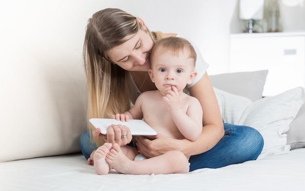 Frau sitzt mit ihrem Baby auf dem Sofa und benutzt Tablet-PC