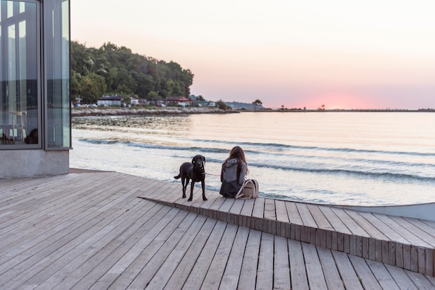 Frau sitzt mit ihrem Hund am Strand