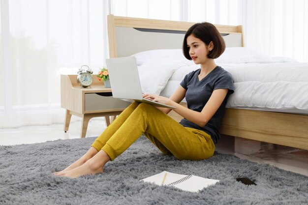 Frau sitzt und benutzt Computer im Schlafzimmer
