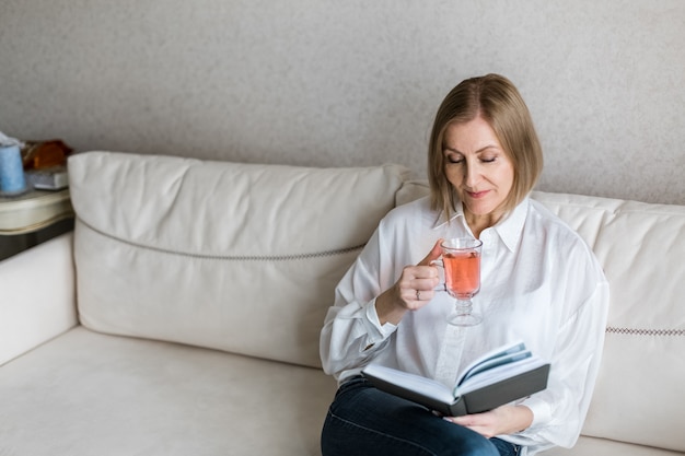 Foto frau sitzt und hält ein buch in der hand und trinkt.