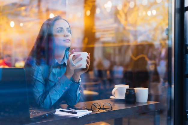 Frau sitzt vor dem Fenster und trinkt Kaffee