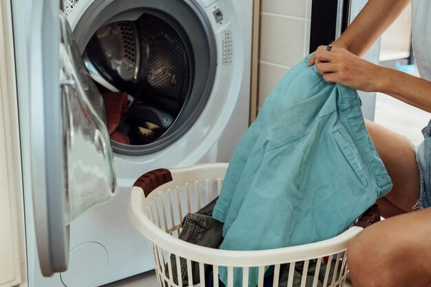Frau sitzt vor der Waschmaschine und lädt sie mit schmutziger Wäsche