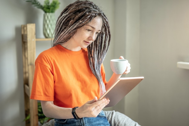 Frau sitzt zu Hause mit einer Tasse Kaffee und liest mit einem Tablet die Nachrichten