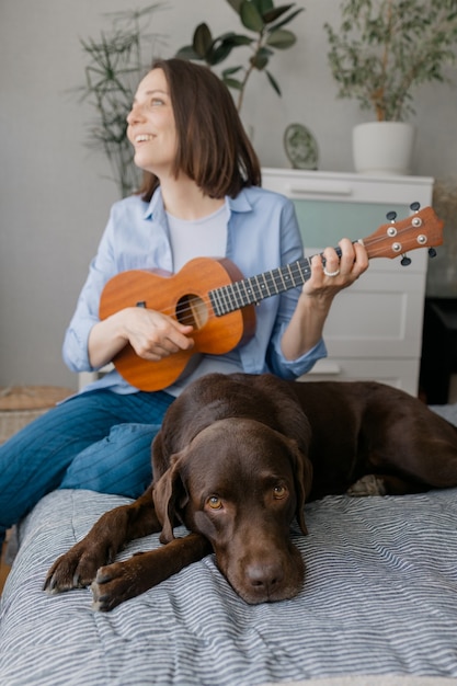 Frau spielt Gitarre oder Ukulele mit ihrem Hund