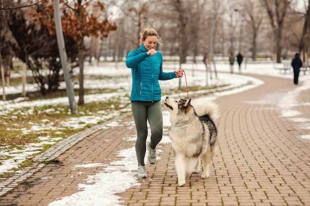 Frau spielt mit ihrem Hund beim Spazierengehen im Park an einem verschneiten Wintertag. Haustiere, Schnee, Freundschaft, Wochenendaktivitäten
