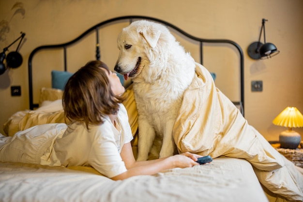 Frau spielt mit ihrem Hund, während sie zusammen auf dem Bett liegt