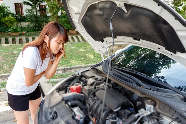 Frau spricht am Handy, während sie auf den Motor des Autos schaut