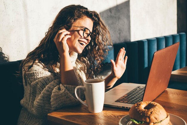 Foto frau spricht und winkt mit der hand während eines videoanrufs im café