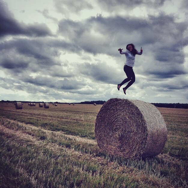 Foto frau springt auf heubal auf gras gegen bewölkten himmel