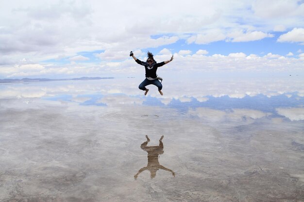 Frau springt mitten in der Luft über einen Salzsee gegen einen bewölkten Himmel in Salar de Uyuni