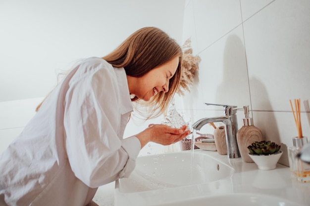 Frau spritzt Wasser über Waschbecken ins Gesicht