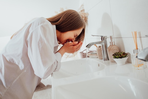 Frau spritzt Wasser über Waschbecken ins Gesicht