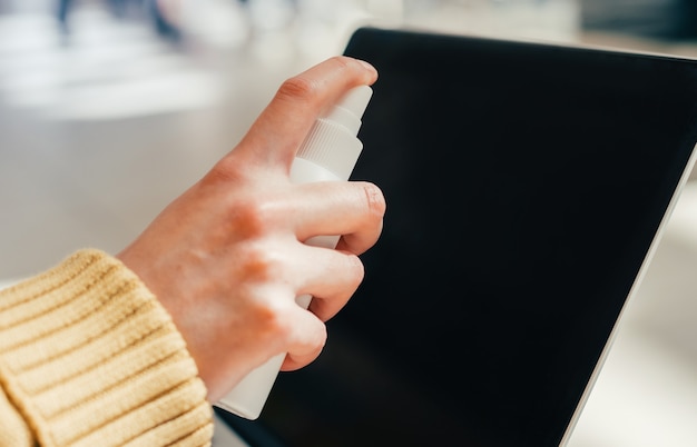 Frau sprüht das Spray auf den Laptop-Bildschirm