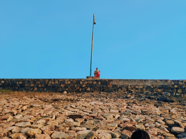 Frau steht an einer Stützmauer vor einem klaren blauen Himmel