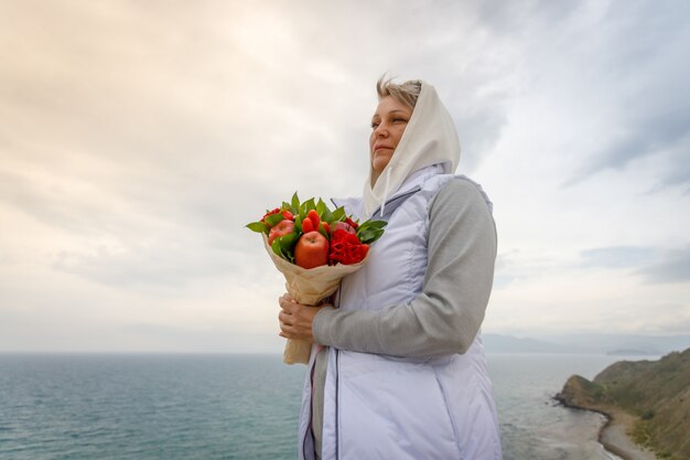 Frau steht auf einem hohen Hügel mit einem Blumenstrauß in ihren Händen