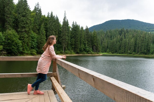 Frau steht auf Teich und blickt auf Bergsee mit Kiefernwald dahinter