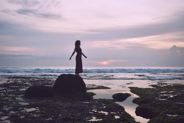 Foto frau steht bei sonnenuntergang auf einem felsen am strand gegen den himmel