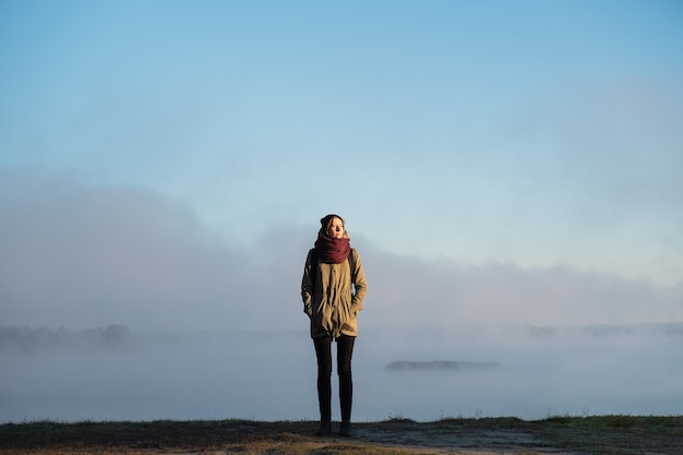 Frau steht im Morgensonnenlicht vor der schönen Naturlandschaft, die mit Nebel bedeckt ist. Weiblicher Wanderer, der aufgehende Sonne im nebligen natürlichen Hintergrund genießt