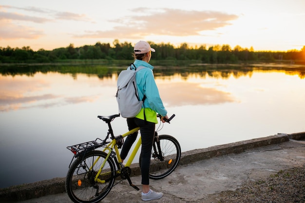 Frau steht im Sommer mit Mountainbike auf der Querfeldeinstraße bei Sonnenuntergang. Direkter Blick