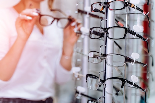 Frau steht mit Brille in den Händen im Hintergrund Optisches Geschäft. Stehen Sie mit Brille. Korrektur des Sehvermögens. Nahaufnahme.