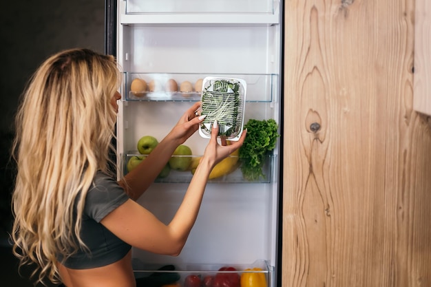 Foto frau steht und schaut in offenen kühlschrank mit produkten